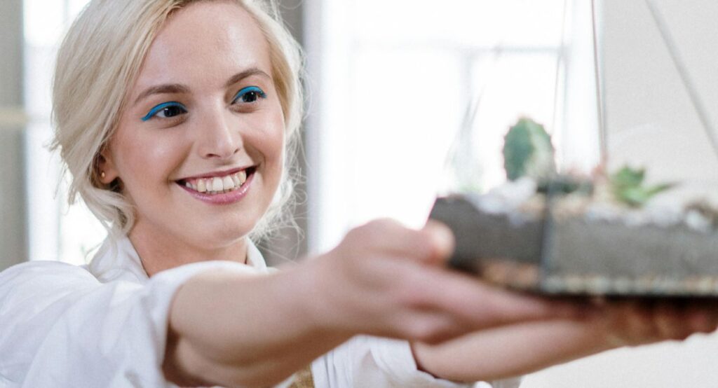 woman holding up a glass-vase terrarium in a light background
