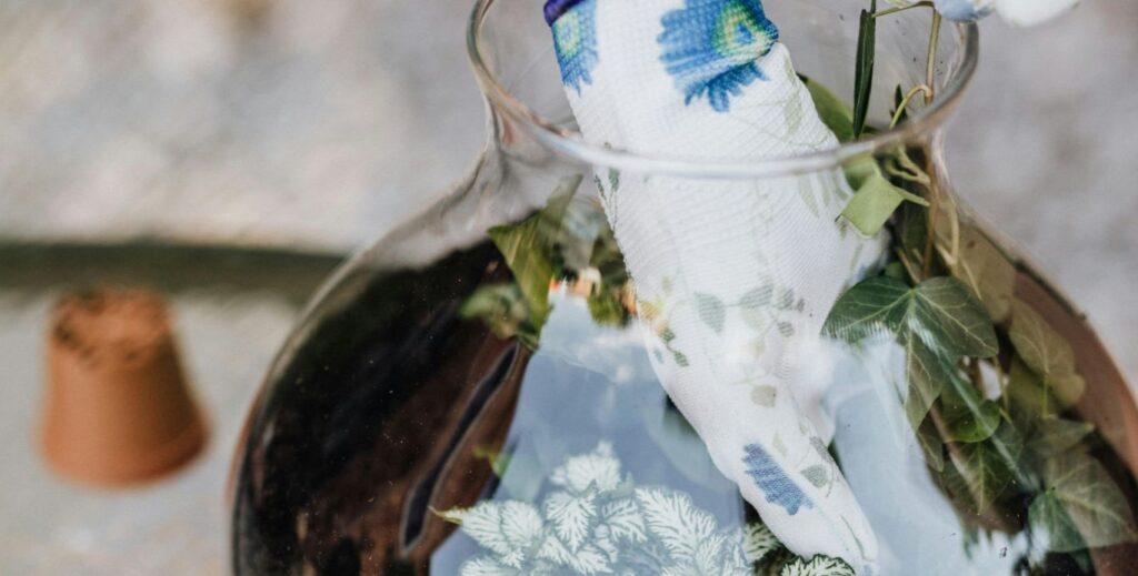 gloved hands mixing earth in a glass vase terrarium