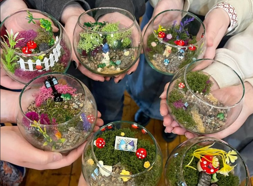 many hands helding glass-vase terrariums with a variety of miniature mushrooms decoration.