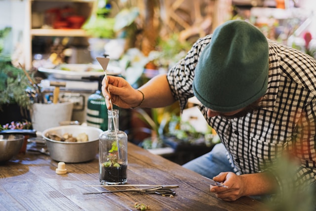 man inspecting a glass-vase terrarium for fungus, using tools